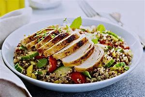 Frango grelhado com quinoa e brócolis, servido em um prato branco, com um toque de cheiro-verde por cima.